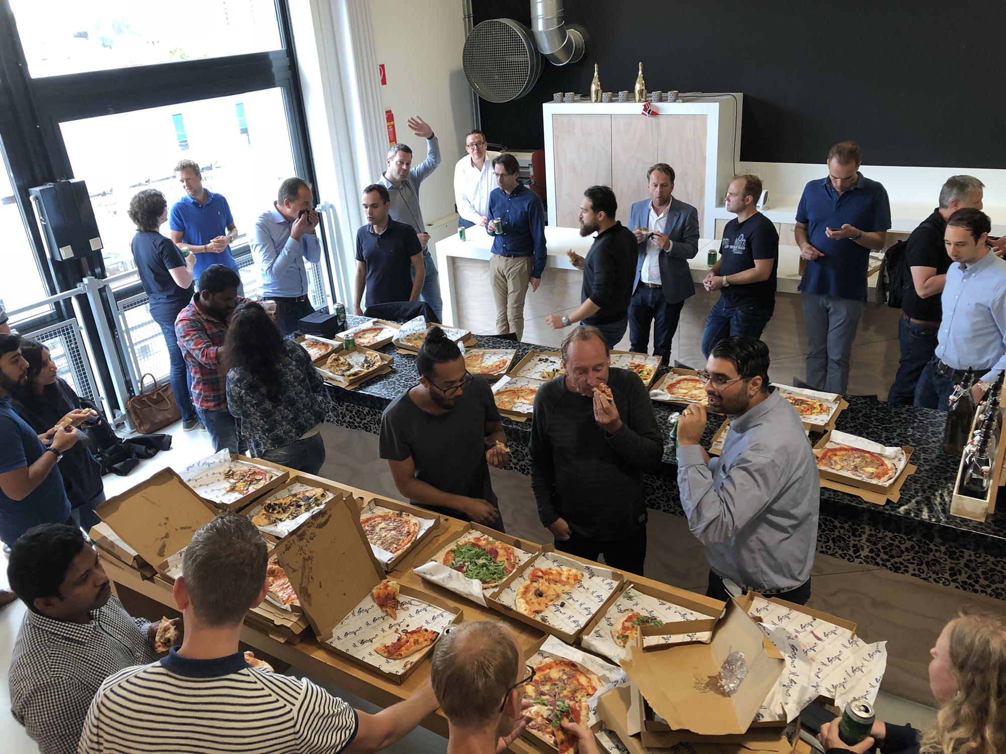 Attendees crowded around tables of open pizza boxes, plates and drinks before a meetup starts