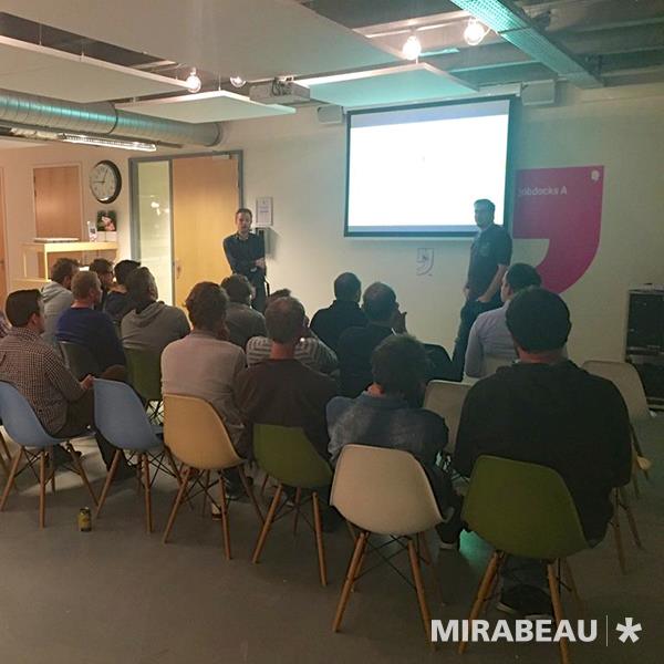 An early meetup: about twenty people on office chairs in a small company meeting room, watching a speaker present